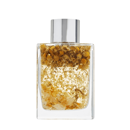 Chamomile Dreams Face & Body Oil - 100ml bottle, featuring a soft, calming design with a subtle floral pattern, resting on a wooden surface surrounded by fresh chamomile flowers. The oil promotes relaxation and nourishment for both face and body.