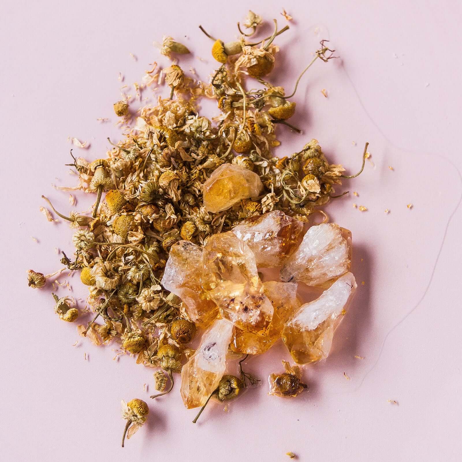 Chamomile Dreams Face & Body Oil ingredients, featuring chamomile flowers and charged citrine quartz on a light pink backdrop.